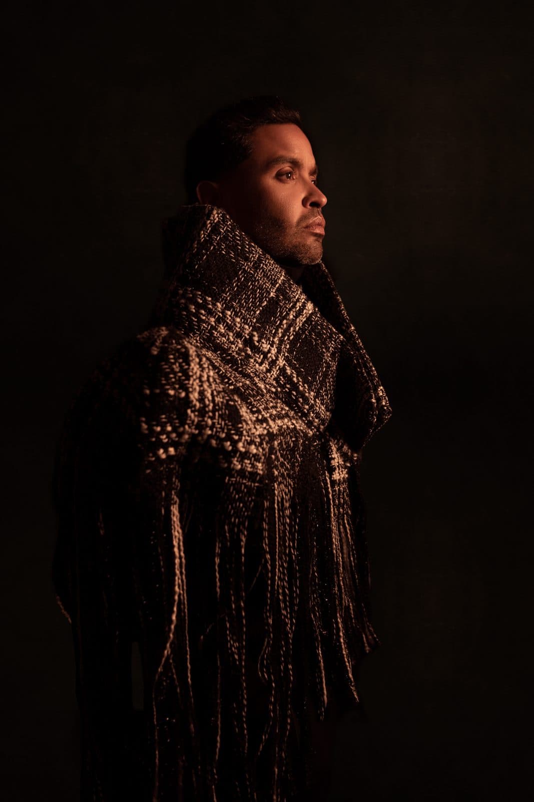 The fringed tweed shawl in profile, the fringe catching a single light