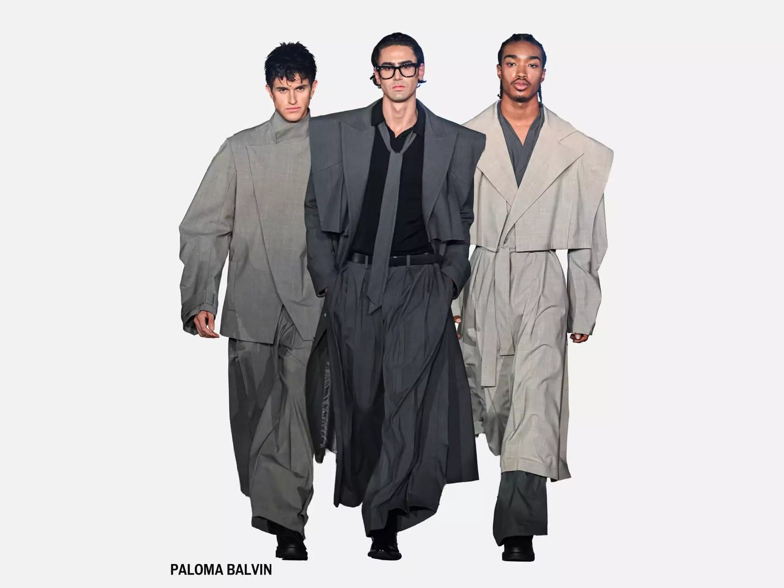 Three models walking in grey tailoring — cropped jackets over wide pleated trousers and a long belted coat