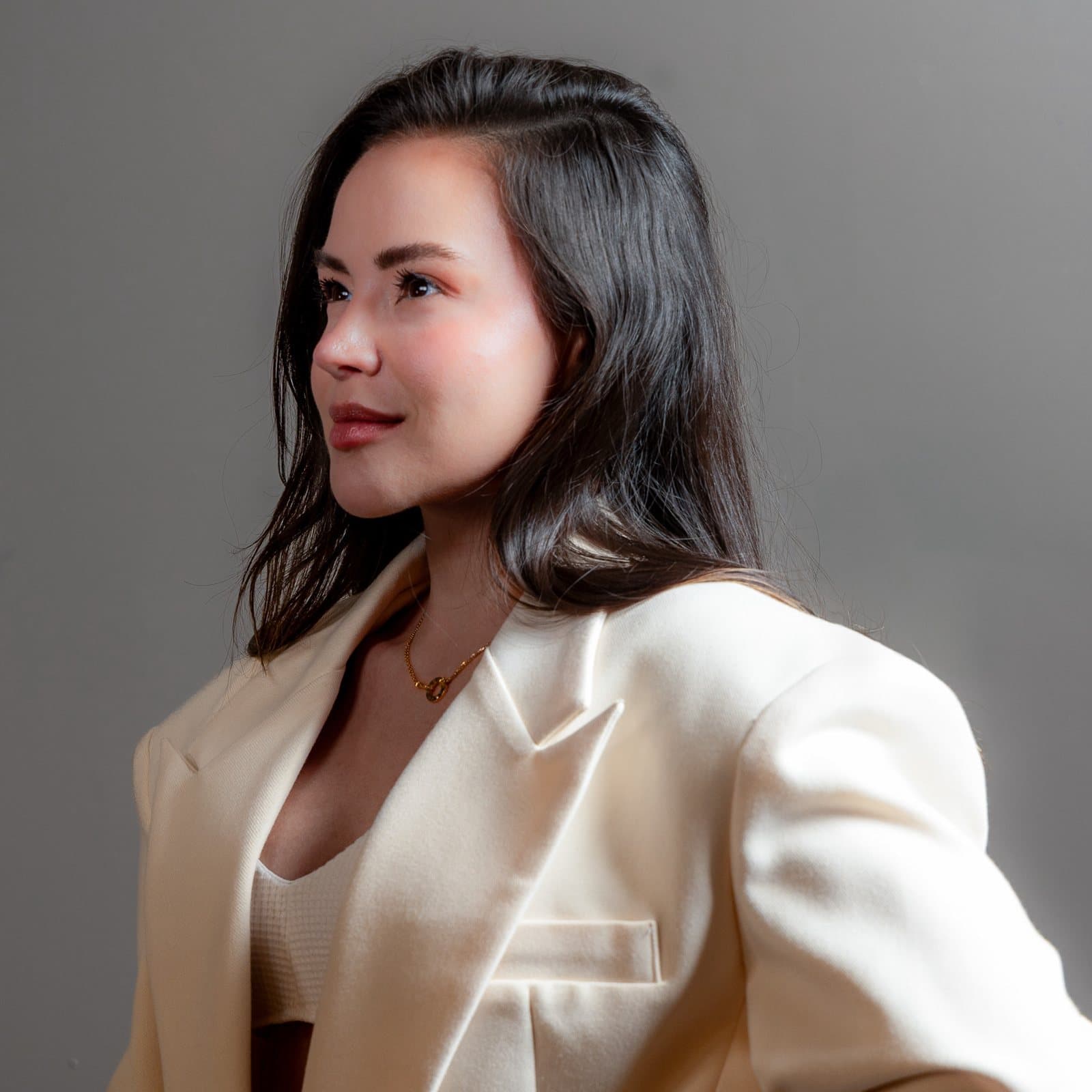Portrait of Paloma Balvin in a cream tailored blazer, turned in profile against a grey ground