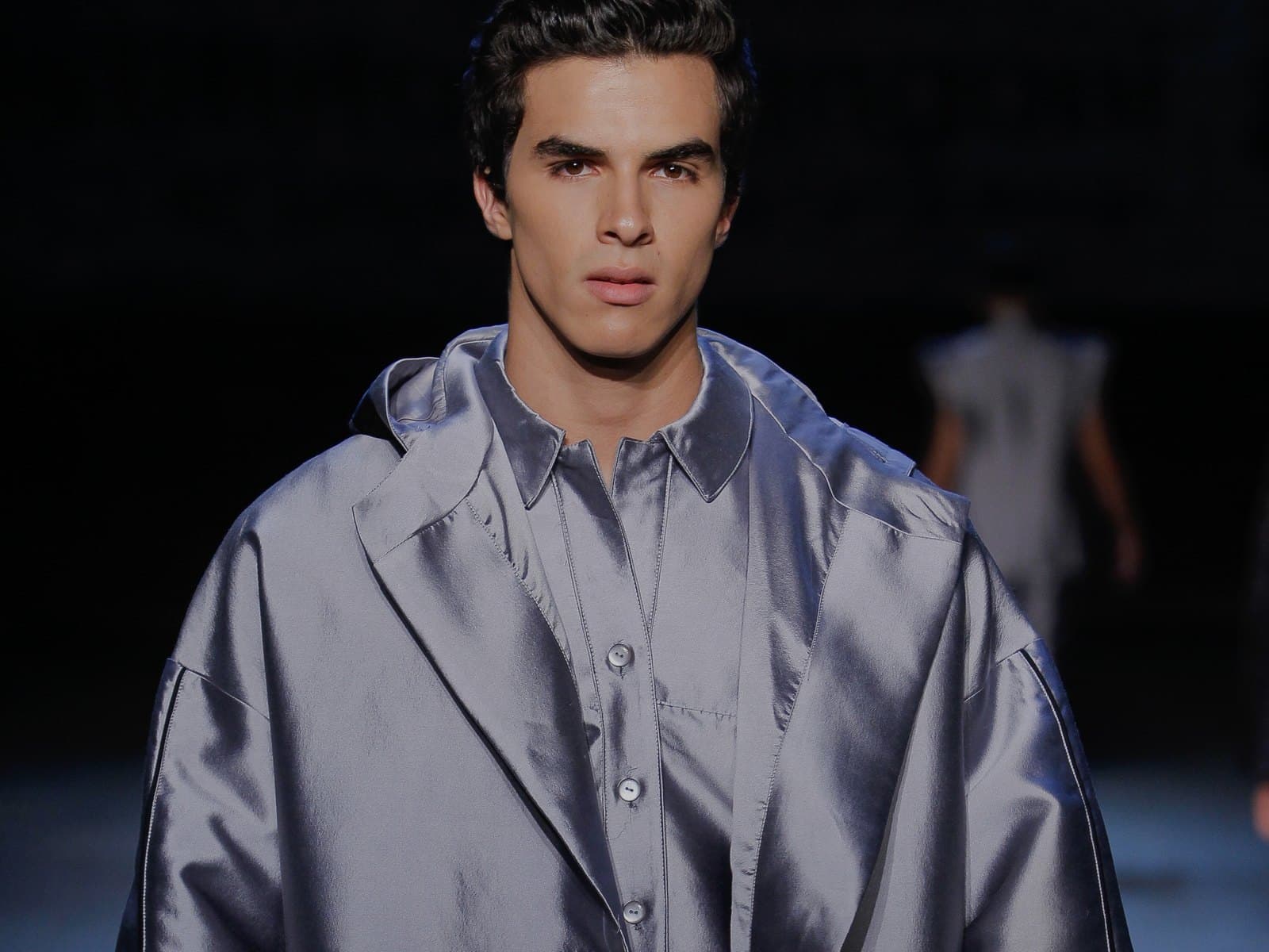 Runway look — an oversized hooded coat in silver satin worn over a matching shirt, taped at the cuff