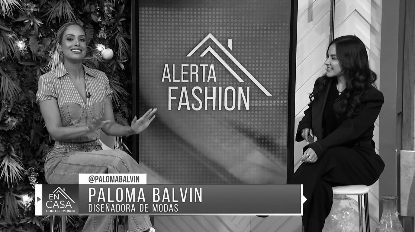 Television still — Paloma Balvin on set beside the host under an Alerta Fashion screen, the lower third naming her diseñadora de modas