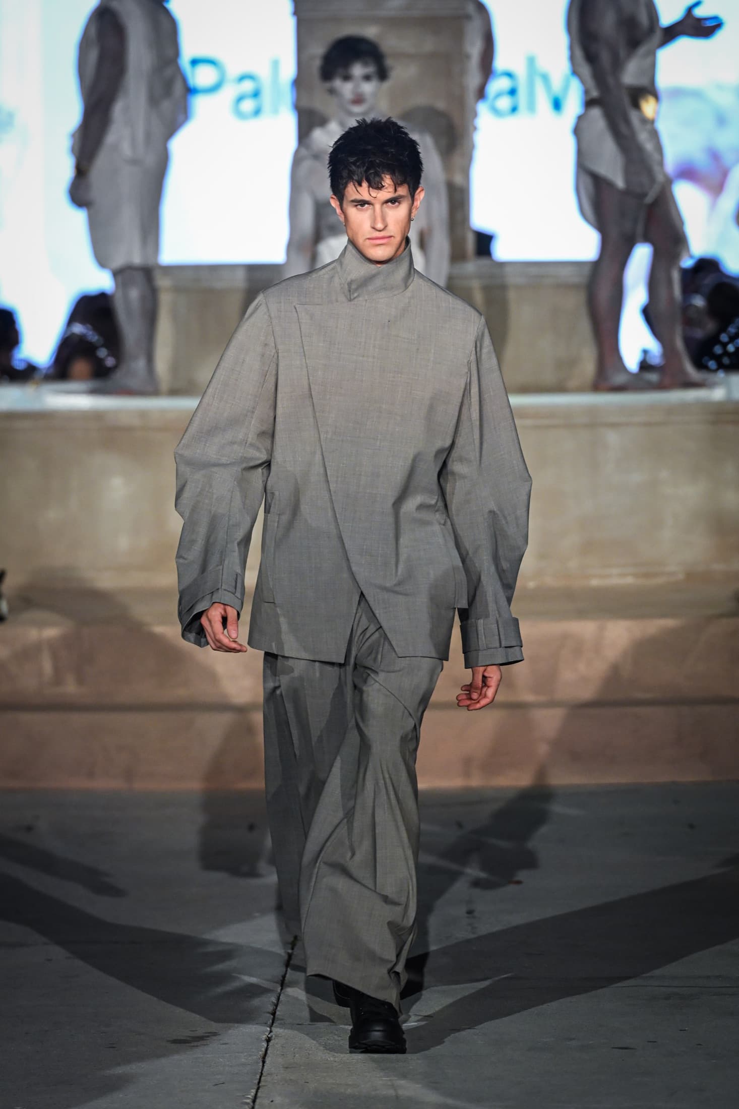 Model in a grey high-neck asymmetric jacket and wide trousers on the runway — Miami Design District