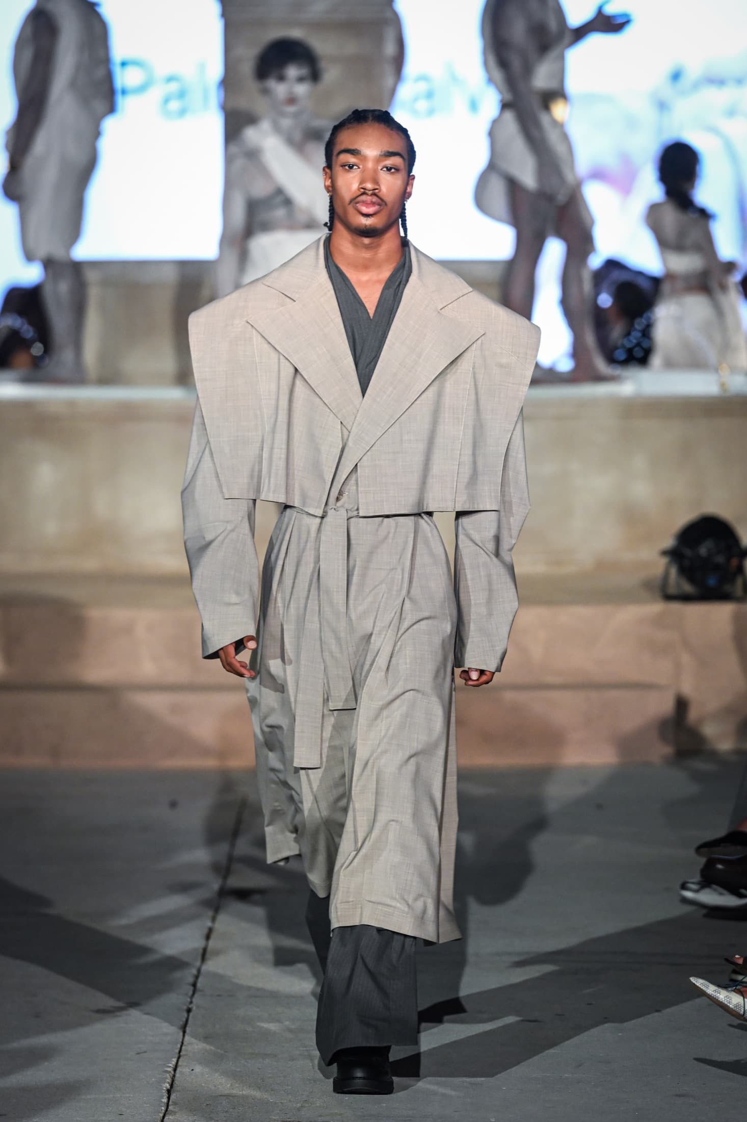 Model in a greige cropped-lapel jacket layered over a long coat and charcoal trousers — Miami Design District