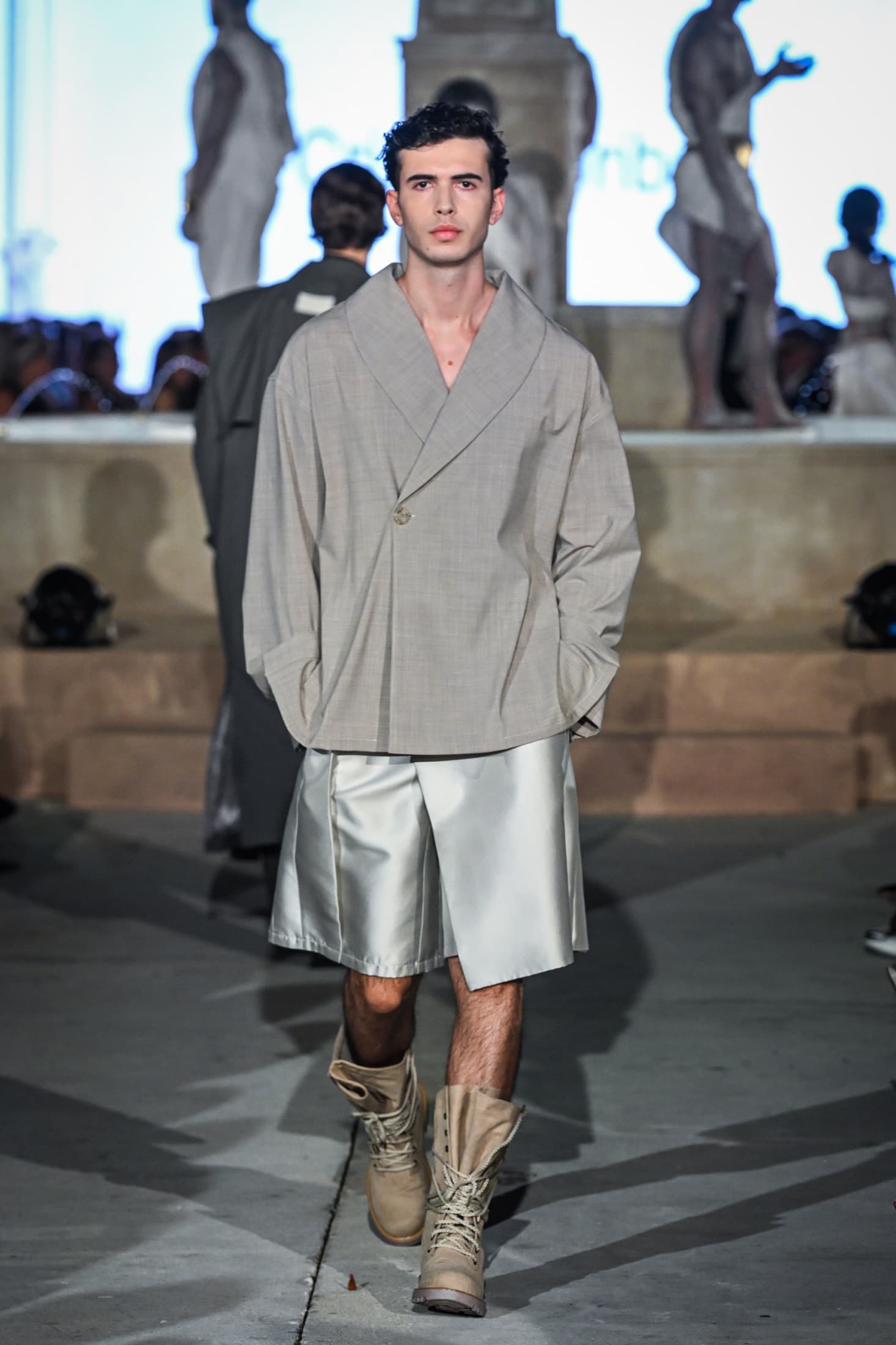 Model in a greige shawl-collar jacket with silver wide shorts and laced boots — Miami Design District