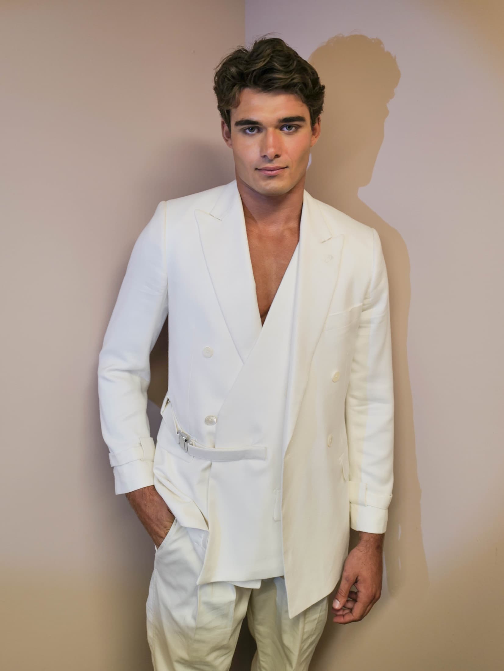 Portrait of the white double-breasted look against a bare wall backstage — Miami Design District