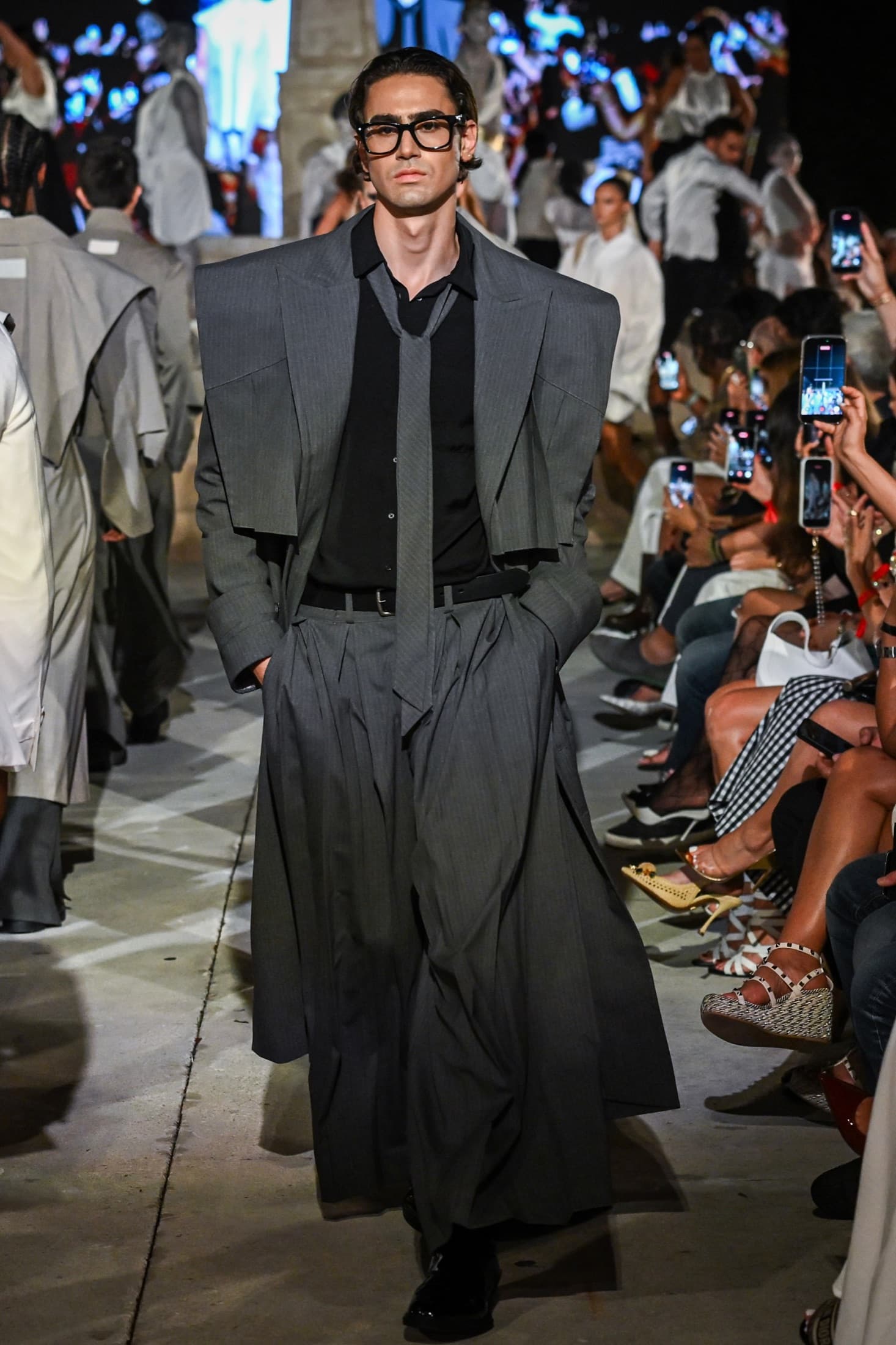 The charcoal suit walking the length of the runway as the audience films from both sides — Miami Design District