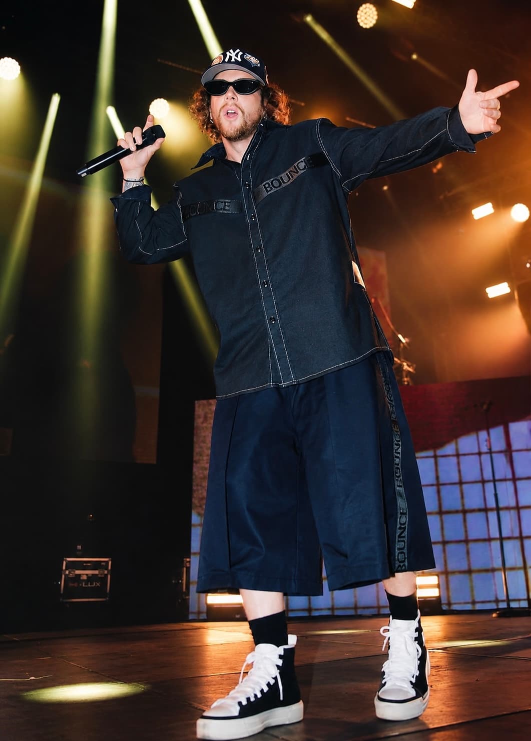 A topstitched denim workshirt cut long over wide pleated denim culottes, worn on stage